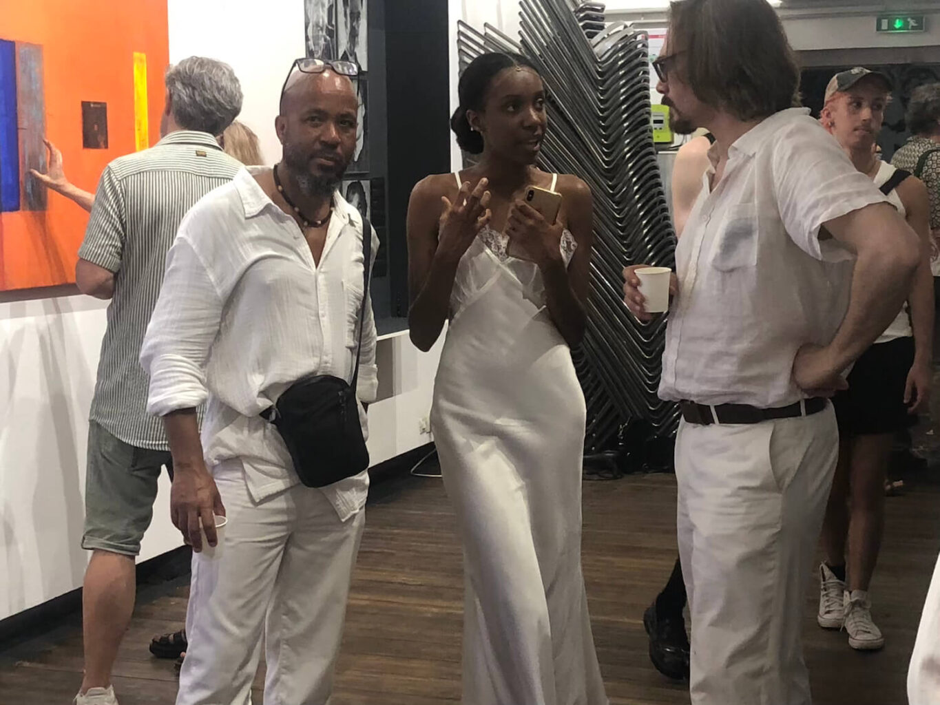 Photographie couleur, élégante jeune fille noire en robe blanche entourée de deux hommes habillés eux-aussi en blanc lors d'un cocktail